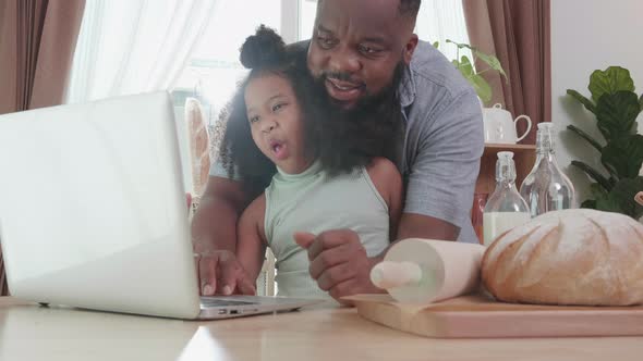 African American dad using a laptop while hug daughter at home  in the kitchen