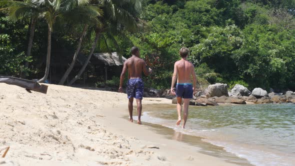 Black and Caucasian Men Walking Together at the Beach on Summer Day. alt
