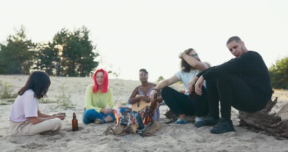 Tired of Studying Students are Relaxing on the Beach By a Lit Bonfire Drinking Beer From Glass alt