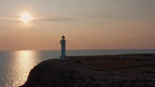 Sun reflected on still sea, white lighthouse on rocky cliff, dolly out alt