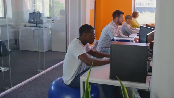 Side view of mixed race business team working on desktop pc at desk in modern office 4k alt