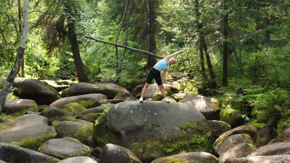 A Girl Does Yoga in the Forest on a Big Stone alt