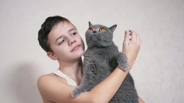 Smiling Child is Holding Hugging Kisses a Fluffy Cat in Her Arms in Room alt