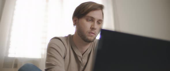 A close up of a young man sitting in bed and working on a computer.  alt