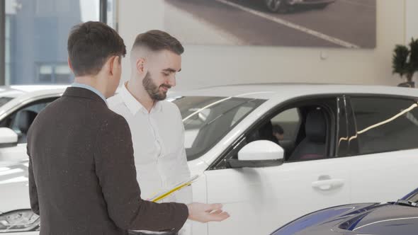 Handsome Businessman Talking to Salesman at Car Dealership alt