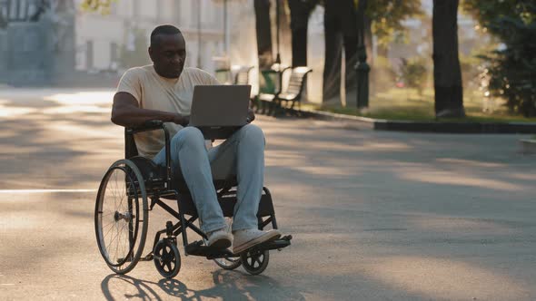 Adult African American Black Man with Disabilities Sitting Outdoors in Summer Park Alone Using alt