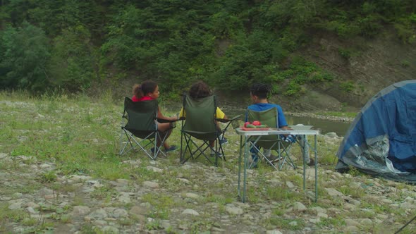 Rear View of Happy Diverse Multiracial Tourists Relaxing at Camping at Mountain Riverbank alt