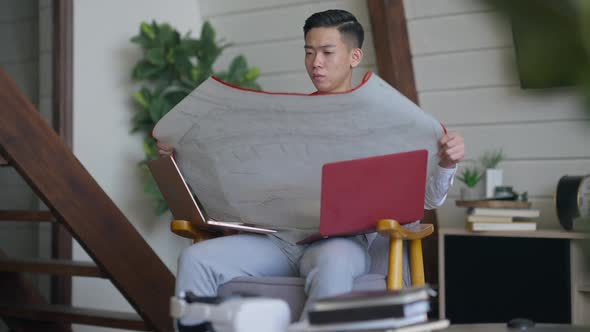 Professional Asian Architect Analyzing Project Plan Sitting in Home Office Living Room Thinking alt