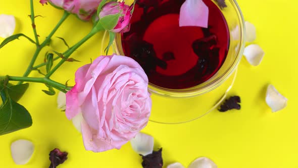 A Cup of Hibiscus Tea with Floating Tea Leaves and a Petal Spinning on a Yellow Background Next to