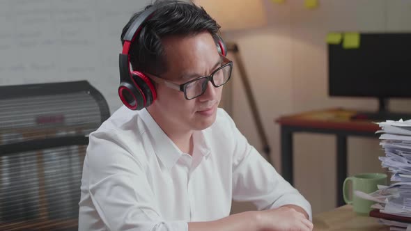 Close Up Of Asian Man Wearing Headphones And Listening To Music After Working With Documents alt