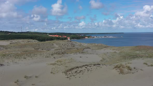 Aerial footage of city of Nida, Lithuania in the distance with sand dunes in the foreground