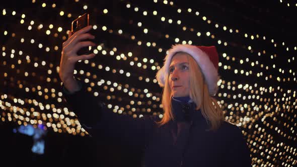 young beautiful blonde in Santa Claus hat, talking on video link in her phone alt