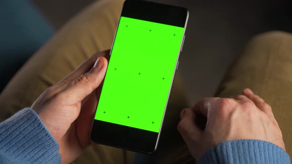 Man Using Smartphone with Green Mockup Screen in Vertical Mode alt