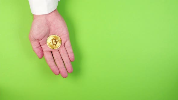 The hand of a young successful trader or broker in a white shirt holds a golden bitcoin