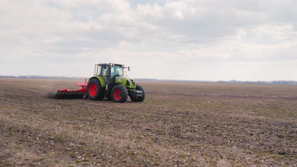 Tractor Working in a Field in the Foreground of Uncultivated Land for Sowing alt