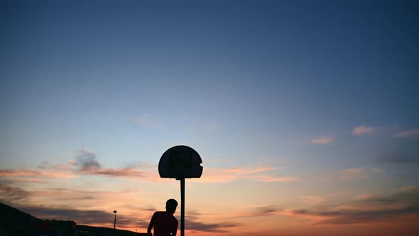 Silhouette of Young Boy Shooting Hoops at Night