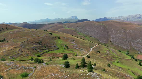 Aerial View of Arid Country Land Some Green Bushes and Trees Blue Sky Mountain in the Horizon Dirty alt