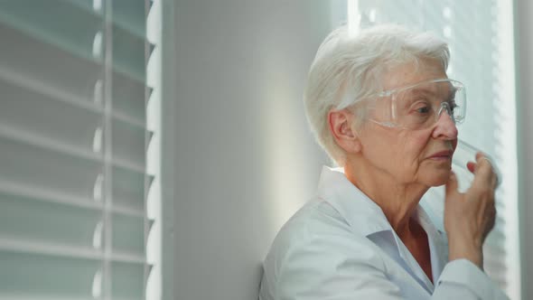 Tired skilled lady doctor in robe with goggles takes off surgical mask alt