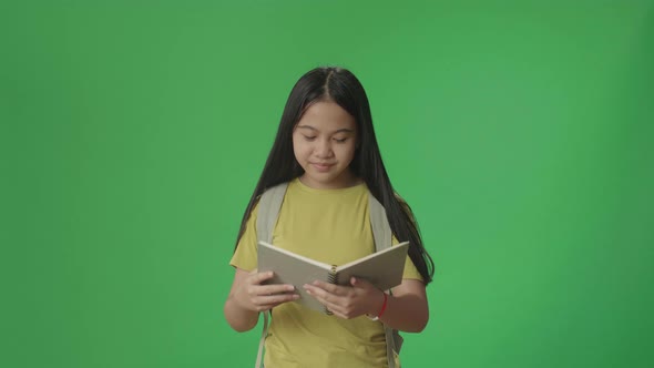 Asian Girl Student Holding And Looking Book While Walking To School On Green Screen Chroma Key alt