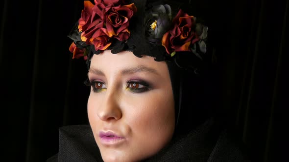 Professional Girl Model with Beautiful Makeup Poses in a Black Cap and Wreath on Her Head in Front