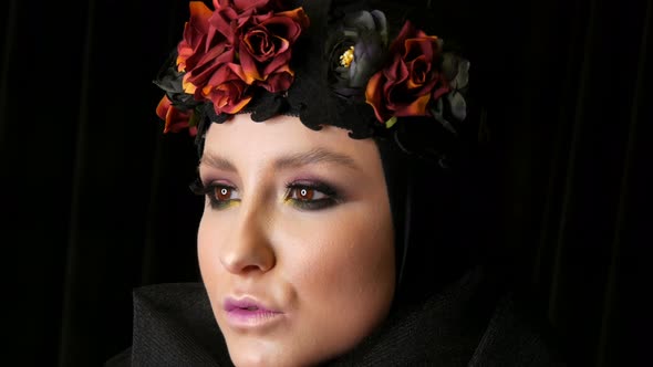 Professional Girl Model with Beautiful Makeup Poses in a Black Cap and Wreath on Her Head in Front alt