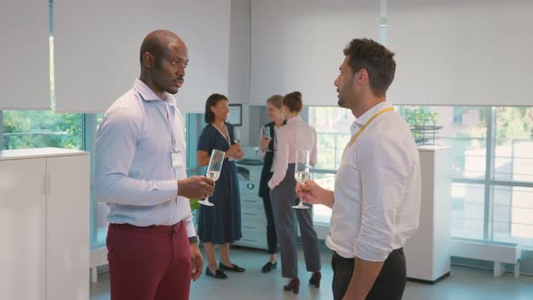 Side View of Cheerful Multicultural Businessmen Holding Champagne Glasses and Talking in Office alt