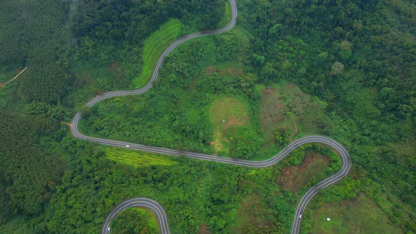 Aerial view over a winding road in the mountains of a tropical forest, Thailand. alt