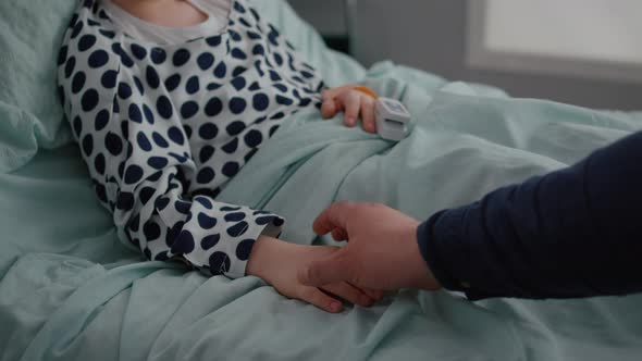 Close Up of Father Sitting with Sick Daughter in Hospital Ward Holding Hands alt