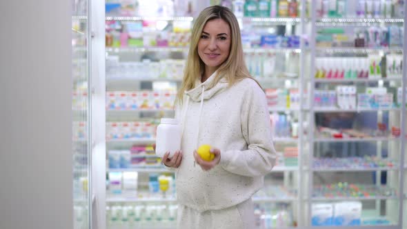 Charming Smiling Pregnant Woman Advertising Multivitamin Complex in Pharmacy Juggling Lemon Fruit alt