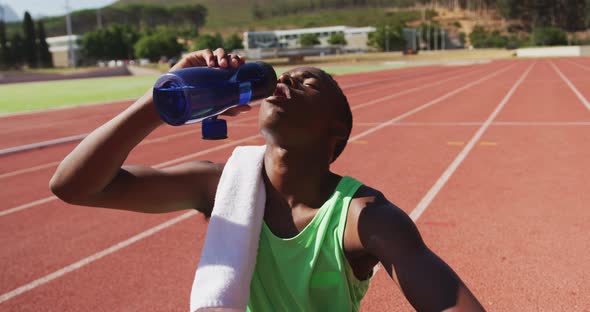 Disabled mixed race man with prosthetic legs sitting on a race track and drinking water alt