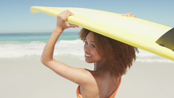 African American woman holding surfboard on her head alt