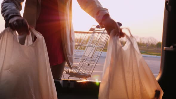 A Woman Stores Packages From a Store in a Car Trunk in a Parking Lot alt