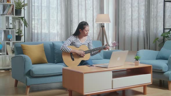 Asian Woman Having Video Call On Laptop And Playing A Guitar At Home alt