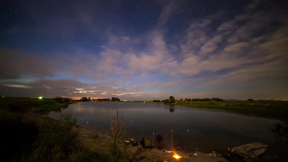 Time lapse at dusk overlooking lake with fishermen and traffic lights alt