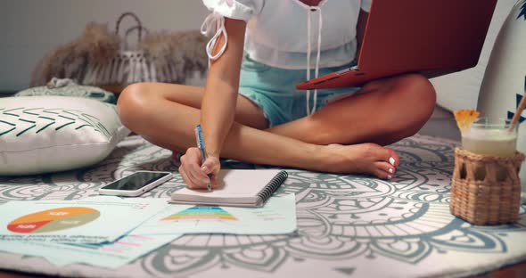 Freelance Woman She Sits on the Carpet and Types on Lap Top Computer and Writes Notes Into Notepad alt