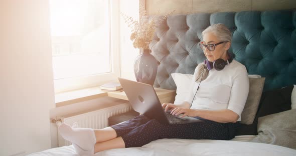 Elderly Woman Typing on Laptop in Bedroom