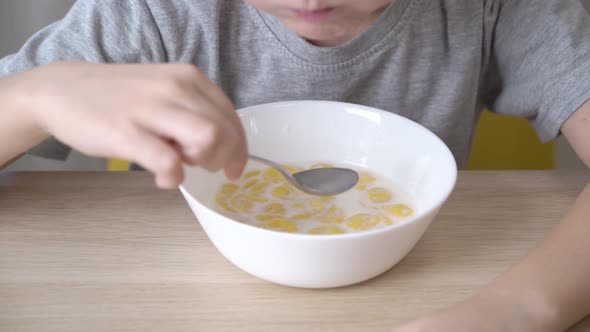 Satisfied little boy eating cereal with milk for breakfast. alt