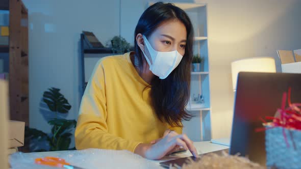 Young Asia businesswoman wear face mask check purchase order on smartphone and stock in computer.