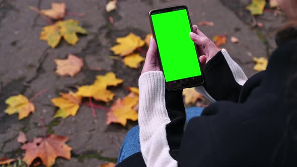 Girl uses a smartphone with a green screen, sitting on a park bench, top view, 