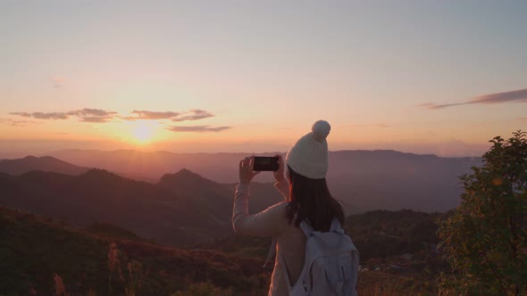 Happy young woman traveler taking photo with smart phone at the beautiful sunset
