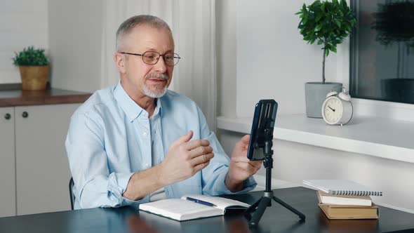 A Male Teacher Records a Live Broadcast on a Smartphone Camera at Home