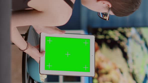 Young Woman Sitting on Sofa Holding Vertical Digital Tablet with Green Screen Watching Online Social alt