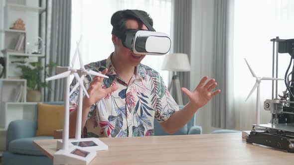 Asian Man Wearing Vr Glasses While Experimenting With Wind Turbine Model And 3D Printer At Home alt