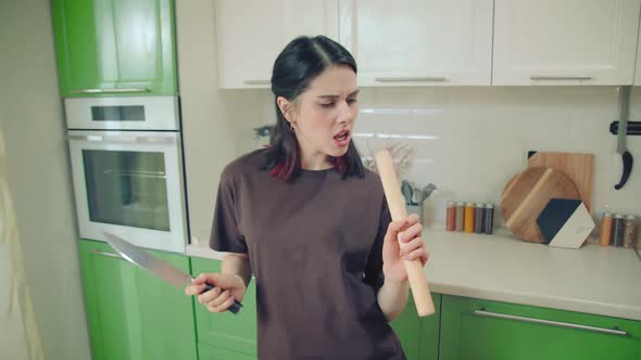 Young Woman Singing and Dancing with Knife and Roller at Home Kitchen