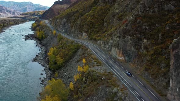 Blue Car Drives Along the Road in the Mountains Along the River alt