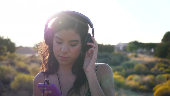 A beautiful young hispanic woman holding a smartphone listening to sad or serious music on headphone alt