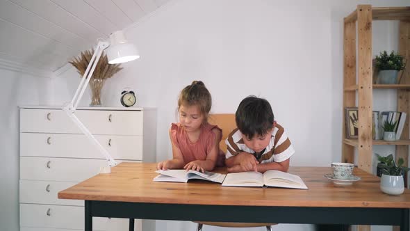 A Boy and a Girl are Reading a Book Sitting on a Table