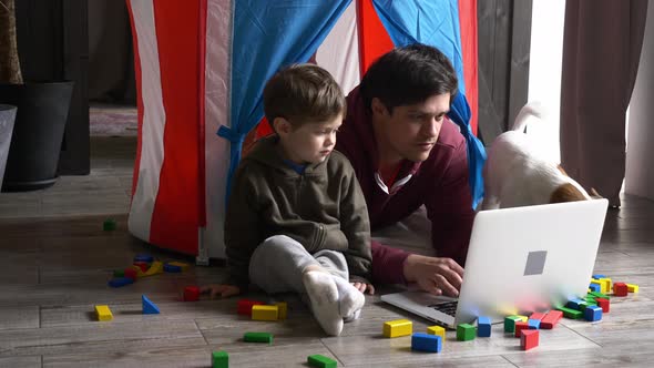 Father and son using laptop computer and lying in a small children's house alt