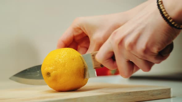 Hands with Knife Cutting Lemon on the Kitchen Board alt