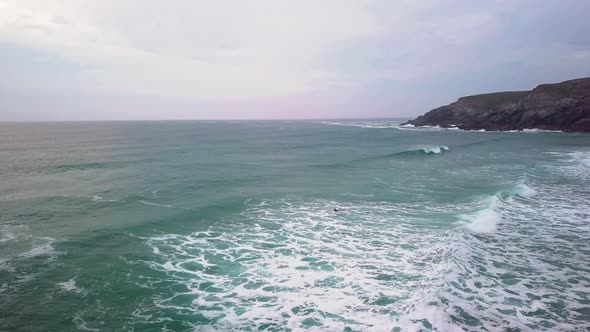 Surfer swimming through choppy waves alongside headland. Drone-shot. alt